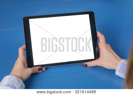 Woman Sitting And Looking At Digital Tablet Computer Device With White Blank Screen On Blue Wooden T