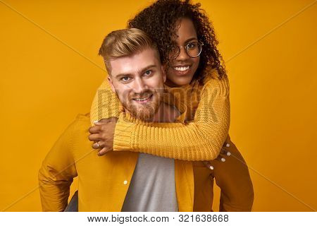 Young Red-haired Man Piggybacking His Dark Skinned Girl Looking With Happy Expression At Camera Isol