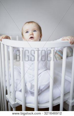 Adorable Baby Girl In Co-sleeper Crib Attached To Parents Bed. Little Kid Sitting In Cot