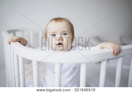 Adorable Baby Girl In Co-sleeper Crib Attached To Parents Bed. Little Kid Sitting In Cot