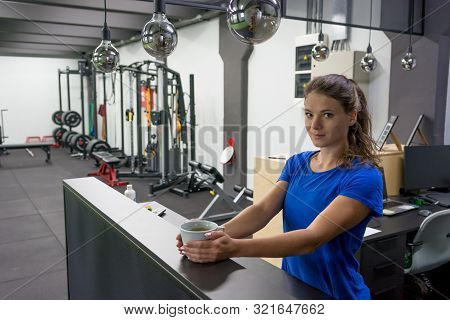 Female Fitness Assistant Greeting You At Homely Gym Bar With A Cup Of Organic Tea.