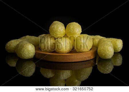 Lot Of Whole Salted Yellow Corn Puff On Bamboo Coaster Isolated On Black Glass