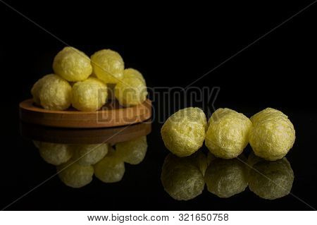 Group Of Eight Whole Salted Yellow Corn Puff On Bamboo Coaster Isolated On Black Glass