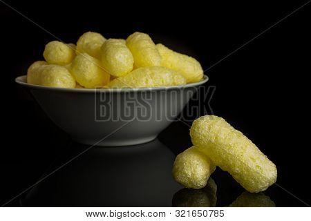 Lot Of Whole Salted Yellow Corn Puff In White Ceramic Bowl Isolated On Black Glass