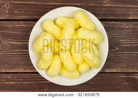 Lot Of Whole Salted Yellow Corn Puff On White Ceramic Plate Flatlay On Brown Wood