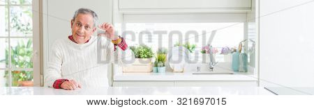 Wide angle perspective of handsome senior man at home smiling and confident gesturing with hand doing size sign with fingers while looking and the camera. Measure concept.