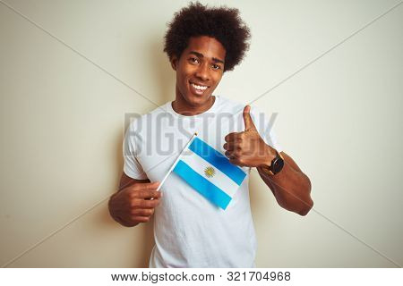 Afro american tourist man holding Argentinian Argentina flag over isolated white background happy with big smile doing ok sign, thumb up with fingers, excellent sign