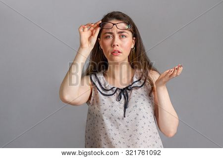 People And Emotions. A Young Brunette In A Blouse, Holding Glasses In Her Hands, Raises Her Hand In 