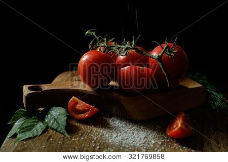 Red Tomatoes Lie On A Wooden Board. Next To The Tomatoes Lies A Leaf Of Wild Grapes And Salt Is Spri