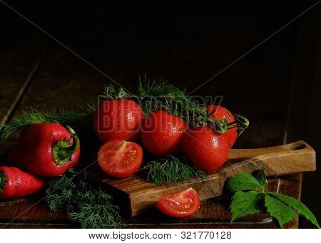 Still Life. Red Vegetables And Greenery  On A Table On A Black Background.
