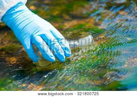 Close Up Of A Scientist's River Drawing Water Into A Research Flask From A Stream