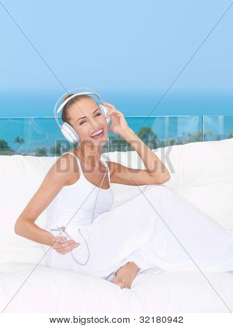 Müzik beyaz koltuk üzerinde kulaklık rahat giyen capcanlı gülümseyen kadın