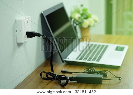 Plug In Power Outlet Adapter Cord Charger On A White Wall Of The Laptop Computer On Wooden Floor