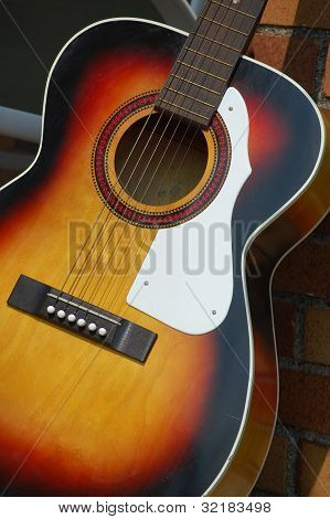 Chitarra acustica colorato appoggiato contro un muro di mattoni.