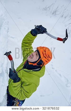 Alpinist Man With Ice Tools Axe In Orange Helmet Climbing A Large Wall Of Ice. Outdoor Sports Portra