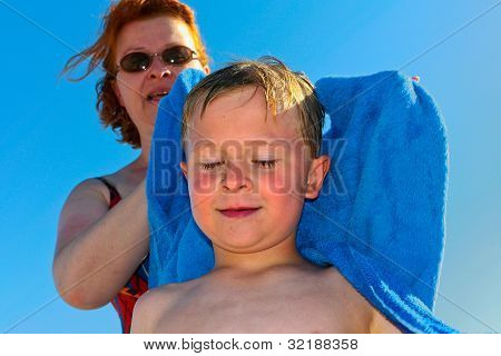 Madre con i capelli rossi e occhiali da sole aiuta suo figlio a secco con un asciugamano in spiaggia
