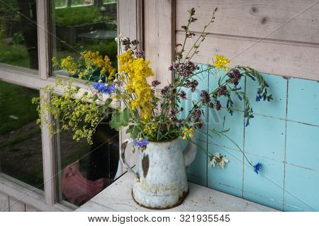 Colourful Mixed Bouquet Of Withering Summer Wildflowers In Rusty Metal Coffeepot On Counter Against 