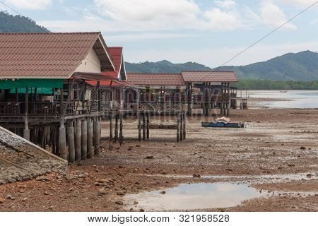 Houses and terraces on the coastline during low tide, with clouds and mountains on the background.