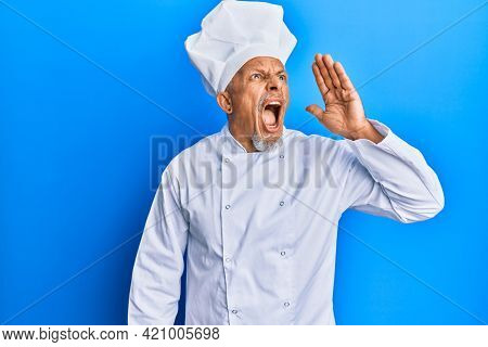 Middle age grey-haired man wearing professional cook uniform and hat shouting and screaming loud to side with hand on mouth. communication concept. 