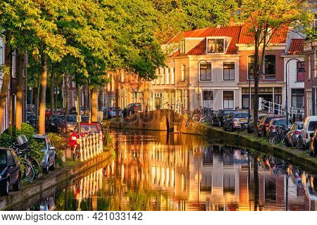 Delt canal with old houses and cars parked along on sunset. Delft, Netherlands