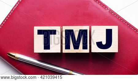 Tmj Made Up Of Wooden Cubes That Stand On A Burgundy Notebook Near The Pen. Business Concept