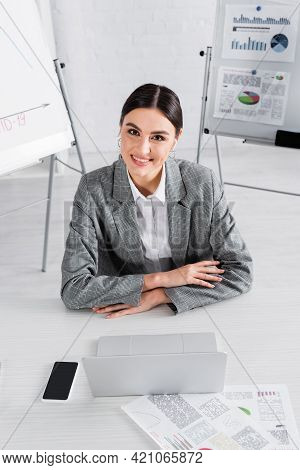 Smiling Businesswoman Looking At Camera Near Gadgets And Documents.