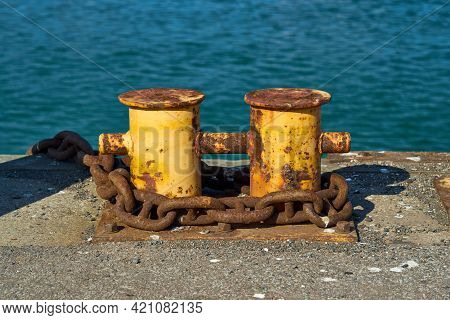 A Double Bitt Mooring Bollard With A Heavy Chain Around It. The Rusty Mooring Bitt Is Used To Anchor