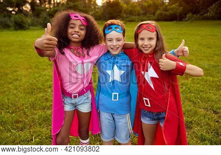 Group Of Multiracial Friendly Kids Wearing Superhero Capes And Masks Hugging Together In Park And Sh