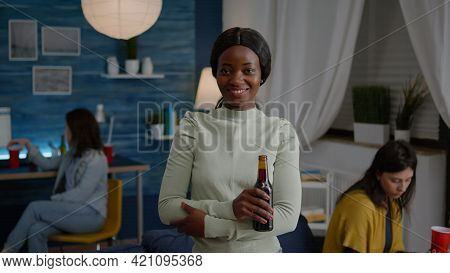 Potrait Of Afro American Woman Smiling Into Camera While Holding Beer Bottle In Hands Late At Night 