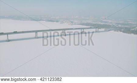 Aerial View Of A Long Bridge Above Snow And Ice Covered River Between Two Parts Of A City. Clip. Win