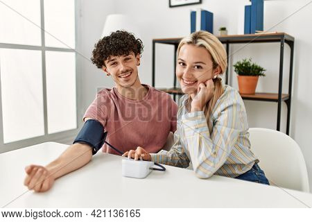 Young couple smiling happy measuring blood pressure using tensiometer at home.