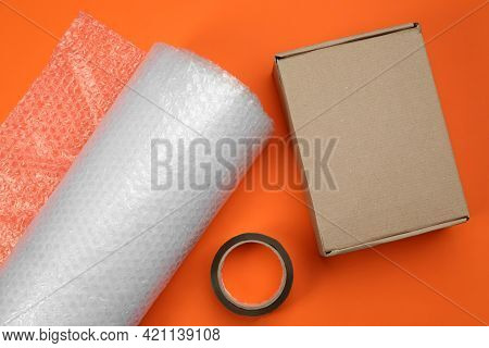 Bubble Wrap Roll, Cardboard Box And Tape On Orange Background, Flat Lay