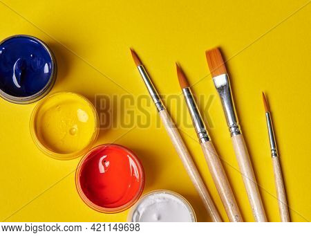 Colored Gouache And Brushes Stands On A Yellow Background