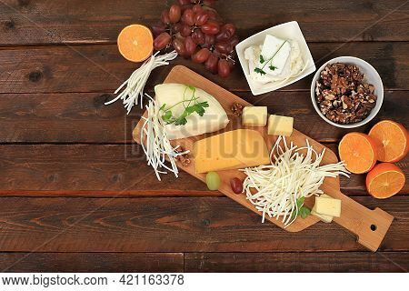 Assortment Of Different Types Of Cheeses, Grapes And Nuts On An Old Wooden Background, Healthy And N