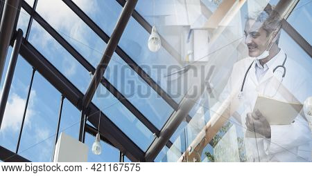 Composition of smiling male doctor with face mask holding file in corridor with double exposure. healthcare and success during coronavirus concept digitally generated image.