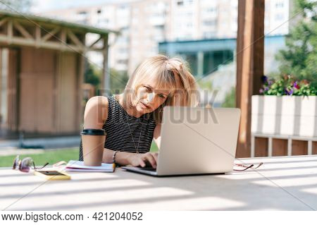 Beautiful Serious Thinking Woman Working At Laptop Outside And Drinking Coffee. Using Computer And O