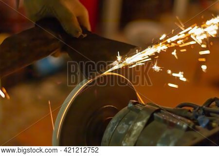 Sharpen The Axe Tool On The Rotating Grinding Wheel, Sparks Fly From The Metal.