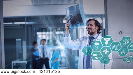 Spot of light and multiple medical icons against male doctor examining x-ray report at hospital. healthcare and medical professionalism concept