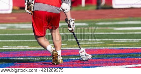 Rear View Of A High School Lacrosse Player Scooping Up The Ball While Runneing Down The Field During