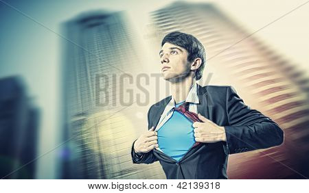 Image of young businessman showing superhero suit underneath his shirt standing against city background
