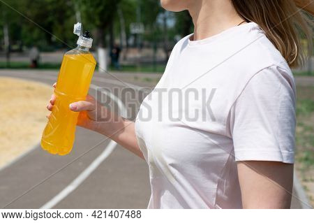 Sportswoman In White T-shirt Holding Bottle With Orange Isotonic Drink On Sports Ground, Summer, Clo