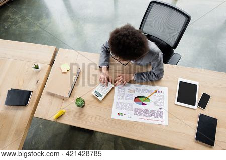 Overhead View Of African American Manager Working With Calculator Near Document And Gadgets.