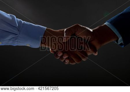Mid section of two businessmen shaking hands against black background. business agreement and professionalism concept