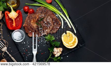 Delicious Prepared Meat Steaks With Seasoning And Herbs On Dark Background.