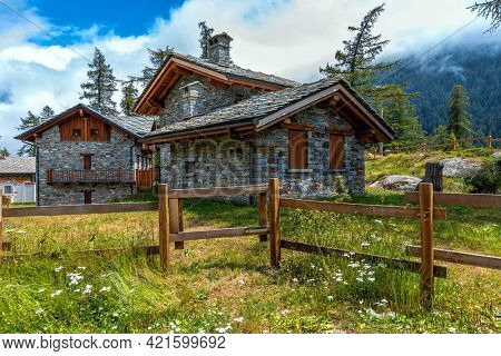 Stone guest houses and wooden fence on green meadow in the mountains in Piedmont, Northern Italy.