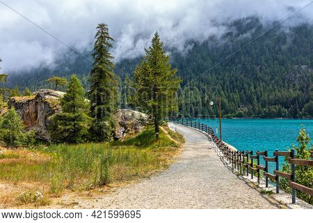 Narrow pathway along Lago di Ceresole and green trees in Piedmont, Northern Italy.