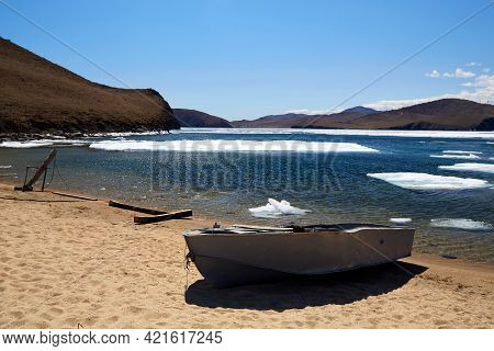 Boat On The Sandy Shore Of Lake Baikal On A Sunny Spring Day. Ice Drift.