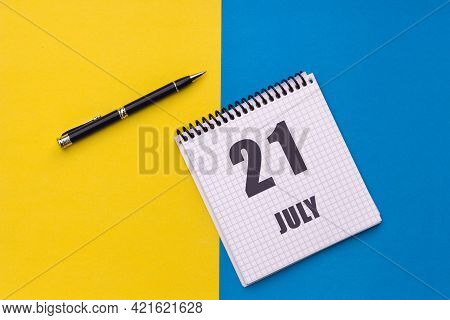 July 21th. Day 21 Of Month, Calendar Date. Notebook With A Spiral And Pen Lies On A Yellow-blue Back