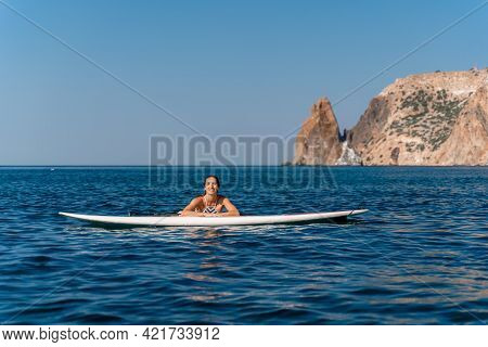 Sporty Girl On A Glanders Surfboard In The Sea On A Sunny Summer Day. In A Striped Swimsuit, He Lies