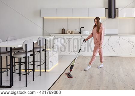 Wet Cleaning With Spray Mop, Young Woman Wipes Floor And Listens To Music Through Wireless Headphone